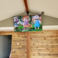 A flat-screen TV mounted from the ceiling displays a colorful children's cartoon with animated characters in a room with wooden walls and vaulted ceilings.