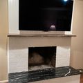 A living room fireplace with white brick surround, dark marble hearth, wooden mantel, and large flat-screen TV mounted above with soundbar