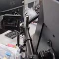 A cluttered computer workstation with a desk-mounted monitor arm, keyboard, and various office supplies including sticky notes and a calculator, with a yellow rubber duck decoration visible on a shelf in the background.