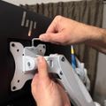 Person installing or adjusting a silver monitor arm mount to the back of a black computer monitor
