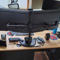 A modern office workspace with dual monitors on an adjustable arm mount, wooden desk, keyboard, mouse, and various office accessories in a professional setting