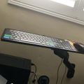 A computer keyboard on an adjustable desk arm mount in an office setting with a window visible in the background