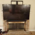 Large flat screen TV mounted above a brick fireplace with glass doors in a living room with hardwood floors