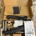 Unboxed monitor mount with gas spring arm, mounting hardware, and instruction manual displayed in cardboard packaging on carpet