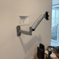 Wall-mounted adjustable monitor arm extending from wall above wooden desk with computer equipment