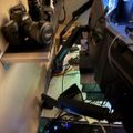 A cluttered desk setup with multiple cameras, lenses, computer monitors, and various electronic equipment with cables and LED lighting