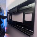 A black wall-mounted media console or shelf unit with two rectangular openings and a top shelf, mounted on a white wall with blue lighting visible on the left side.