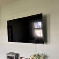 Wall-mounted flat screen TV above decorative storage baskets and a vase with flowers