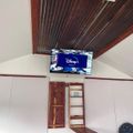 A wall-mounted TV displaying the Disney+ logo in a room with white walls, wooden ceiling beams, and built-in storage shelving