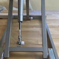 A metal exercise equipment frame with adjustable components positioned on a wooden floor near a window in an indoor setting.
