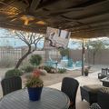 Covered patio with outdoor furniture overlooking a desert backyard with pool, landscaping, and mountain views