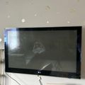 A wall-mounted LG television displaying what appears to be a movie scene, with decorative circular wall decals and a wire shelf visible to the left