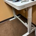 White height-adjustable standing desk with keyboard, mouse, glasses and other office supplies on top