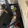 A cluttered desk workspace with computer monitor, lamp, various office supplies, papers, and personal items scattered around