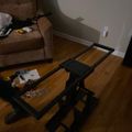 A black adjustable laptop stand or table positioned on wooden flooring in a living room with a brown couch visible in the background