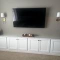Wall-mounted flat screen TV above white built-in cabinet with decorative bowl, flanked by two wall sconces