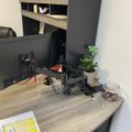 A modern office workspace with a wooden desk, dual monitor setup, small potted plant, and built-in shelving with cabinets above