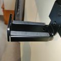 Black metal mounting bracket or clamp attached to equipment, shown in close-up against a white background