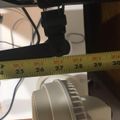 A measuring tape stretched across a workspace showing measurements from 24 to 30 inches, with various electronic equipment and cables visible underneath