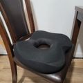 A black donut-shaped cushion placed on a wooden dining chair with a dark leather seat