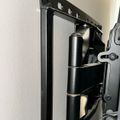 Black adjustable TV wall mount bracket attached to white wall with articulating arm extended