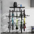 Wall-mounted bike storage rack holding multiple bicycles with a shelf above containing water bottles and a backpack