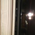 A sliding glass door partially open at night with bright lights visible outside and white interior doors or panels visible on the left side