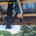 A chainsaw mounted on wooden ceiling beams of an outdoor structure with trees visible in the background