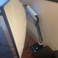 A large curved computer monitor mounted on an adjustable black arm stand positioned on a wooden desk surface