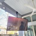 Outdoor patio area with mounted TV screen displaying content, featuring white ceiling beams and modern architectural elements