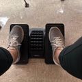 Person's feet in beige sneakers resting on a black foot rest under a desk