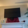Living room with flat screen TV mounted above white fireplace mantel, decorative items on mantel, and houseplant visible to the right