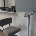 Office workspace with gray chair, white cabinets, adjustable equipment stand, and mirror with items on counter