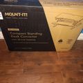 A boxed Mount-It! Compact Standing Desk Converter with 30-inch desktop sitting on wooden flooring