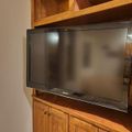 A Samsung flat-screen TV mounted in a wooden entertainment center with shelving above and cabinet doors below