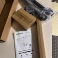Unboxed dual monitor desk mount with instruction manual, mounting hardware, and packaging materials spread on a tiled floor