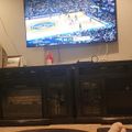 A large TV mounted on a wall displaying a basketball game, with a dark entertainment center below it in a living room setting