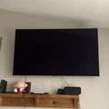 Wall-mounted flat screen TV above a wooden floating shelf with gaming console and decorative items