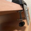 A metal clamp attached to the edge of a wooden desk or table surface