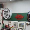 Interior of an automotive garage with various car brand logos and memorabilia on the walls, including Jaguar and Mercedes-Benz emblems, vintage car posters, and garage-themed decorations
