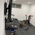 Home gym with exercise bike, dumbbells, and wall-mounted TV in a carpeted room with white walls
