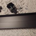 A black turntable or record player with tonearm and cartridge components laid out on a textured surface with leaf pattern wallpaper in the background