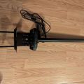 A black adjustable desk clamp or mount with cables attached, lying on a wooden floor