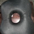 A black donut-shaped cushion with a circular opening in the center, sitting on a wooden chair