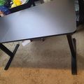 A gray desk with black metal legs positioned on a beige carpet in what appears to be an office or workspace setting