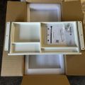 An opened cardboard shipping box containing a white plastic organizer tray with multiple compartments and an instruction manual