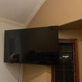 A large flat-screen TV mounted on a wall in a room with windows and wooden blinds