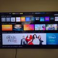 A Vizio smart TV displaying a streaming service home screen with various app icons including Netflix, Prime Video, Hulu, Disney+, and others. The main featured content shows "The Devil Wears Prada" available on Disney+ and Hulu, with promotional images of the cast displayed prominently.