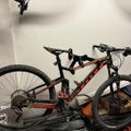 Black and red mountain bike with full suspension parked indoors against a white wall