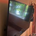 A large flat-screen TV mounted on an orange wall displaying a nature scene with green trees and water, with shelving visible to the right side
